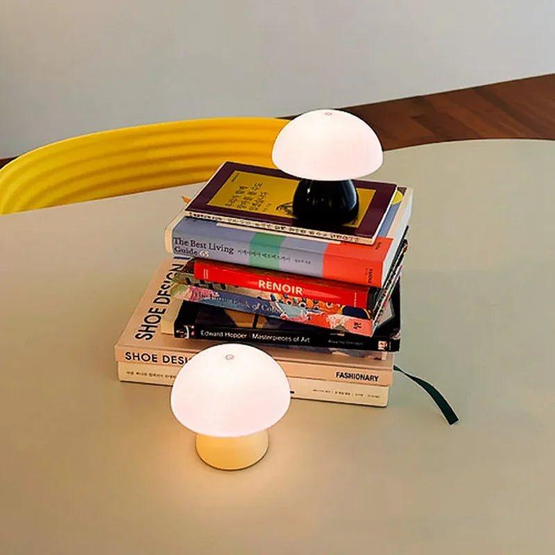 Two small table lamps on a stack of books with a yellow chair and wooden surface in the background.